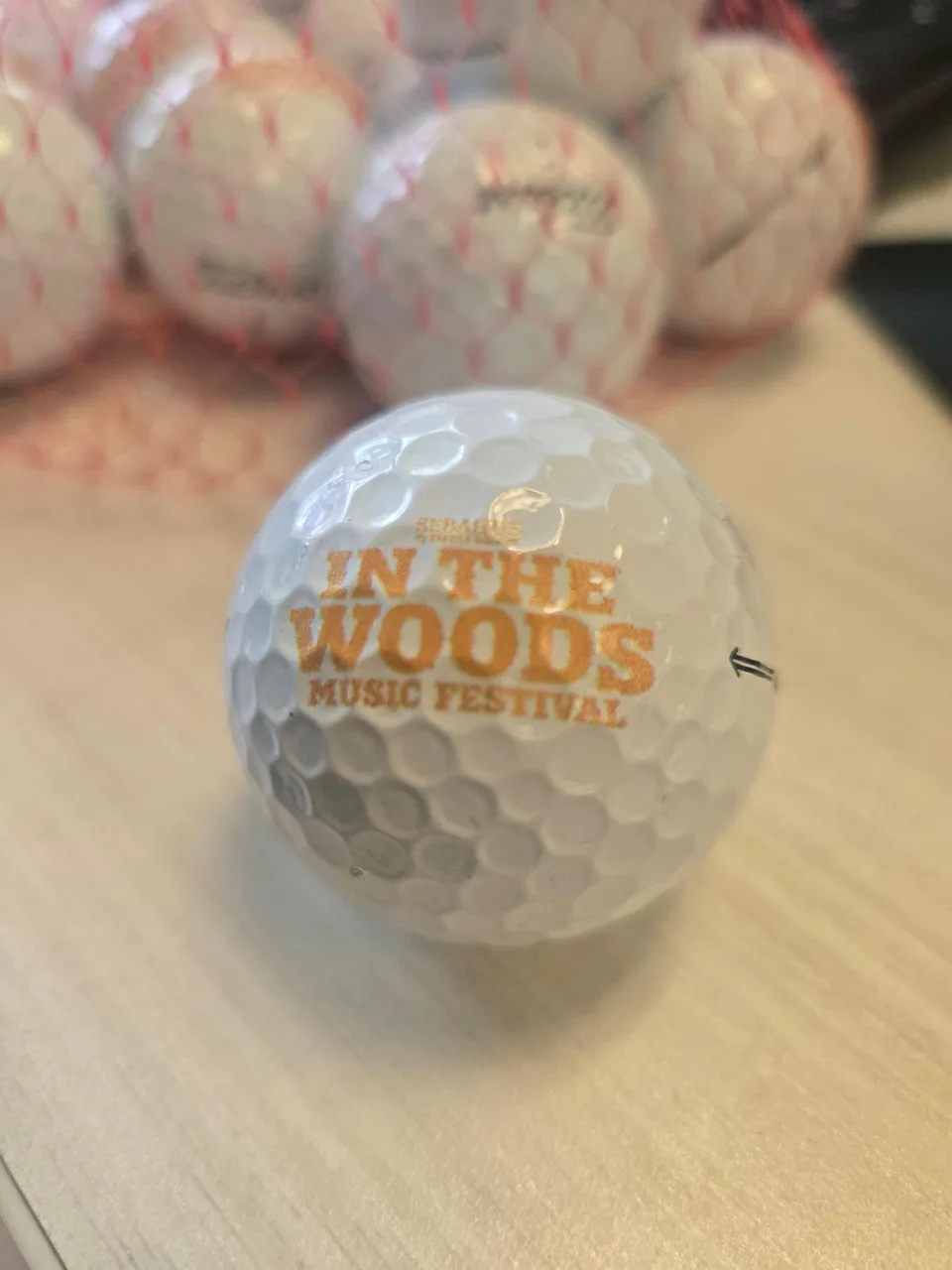 A qualifying white golf ball printed with the orange In the Woods Music Festival logo